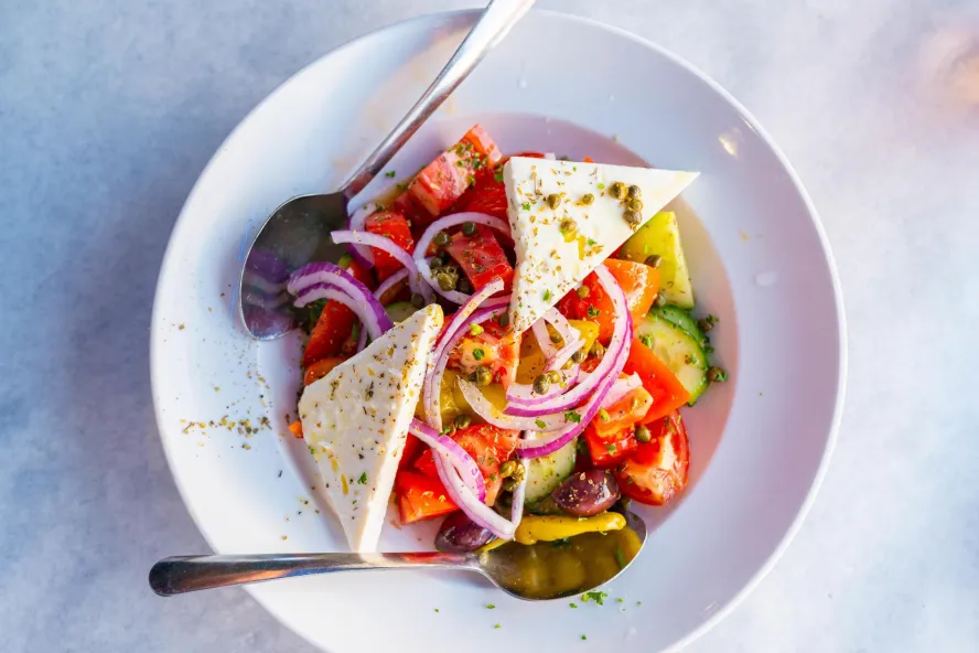 a colorful greek salad with triangle-shaped wedges of feta cheese sprinkled with greek spices