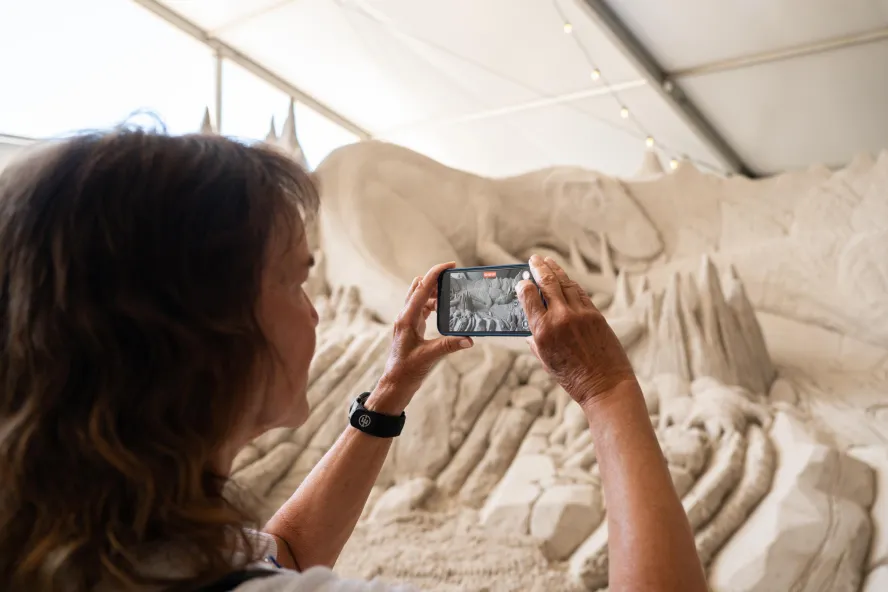A woman taking a photo of a sand sculpture