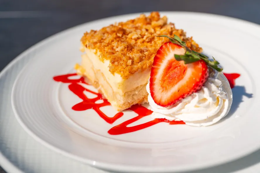 a square cheesecake slice with a crumble top, garnished with whipped cream and strawberries and a drizzle of strawberry sauce
