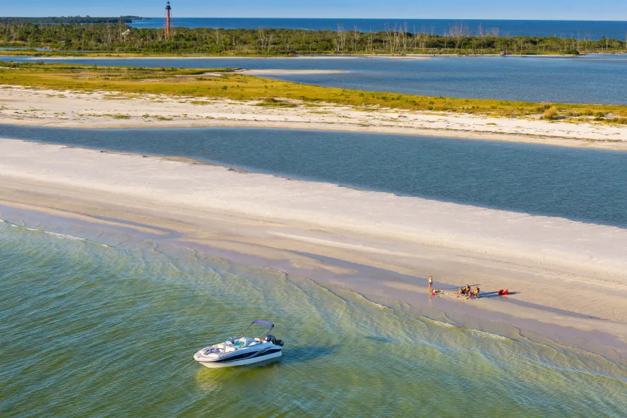 a boat at anchor near a small strip of land where people are relaxing on the beach