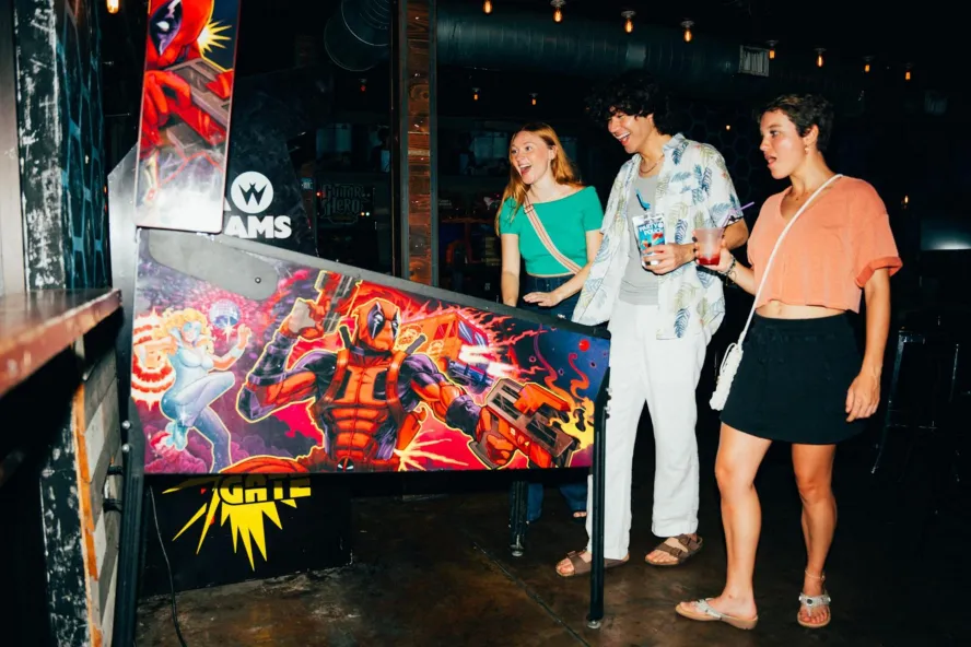 three young people play an arcade game at park