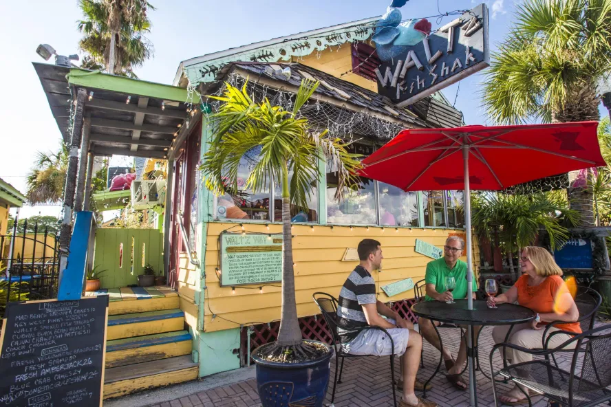 three people at an outdoor table with an umbrella at Walt'z Fish Shak at John's Pass Village & Boardwalk in Madeira Beach