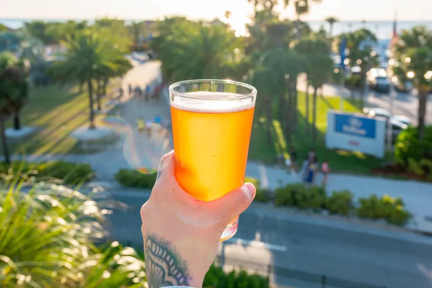 a person holding out a glass of beer while enjoying the distant view of Clearwater Beach