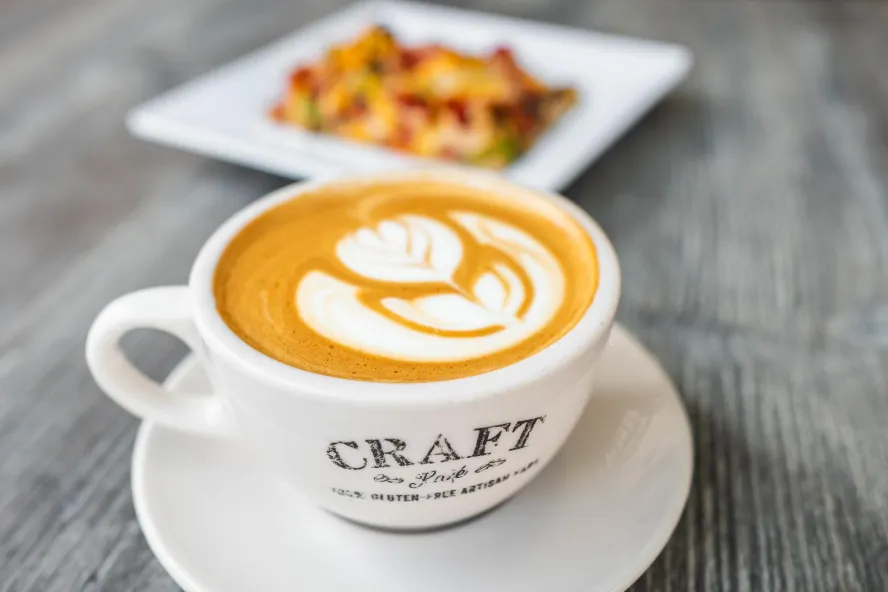 cappuccino with a flower design in a small white mug on a plate, next to a plate of food at Craft Kafe