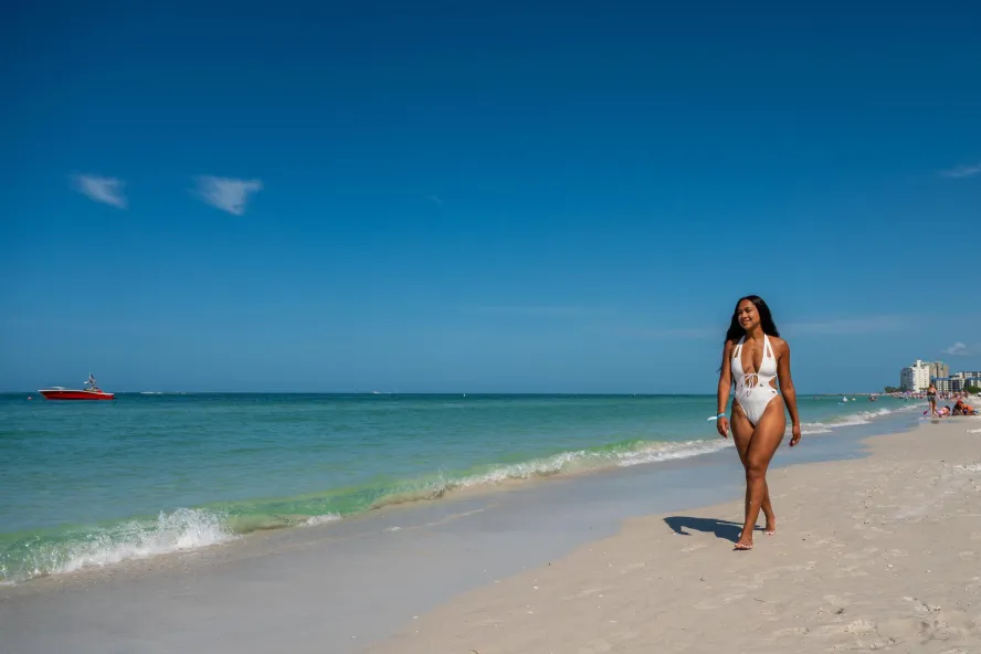 a young woman in a white bathing suit walks on the edge of the water at Clearwater Beach