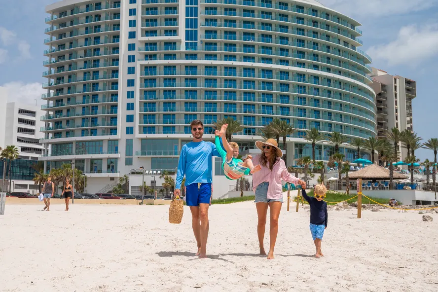 a mom, dad and two kids smile while walking out onto the beach at Opal Sands Resort