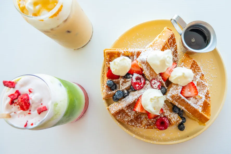 two colorful iced espresso drinks next to a plate of waffles topped with berries at Sugar Baby in Seminole