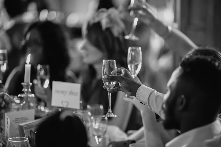 Black and white photo of people at tables toasting with champagne. 