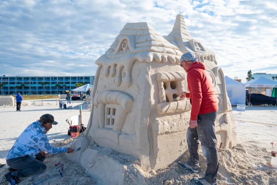 two artists work on a sand sculpture of a house at Sanding Ovations