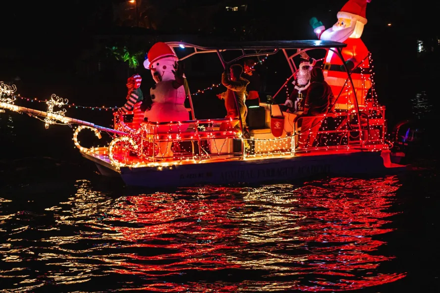 a small boat decorated with holiday lights and blow-up holiday decorations of Santa and a snowman