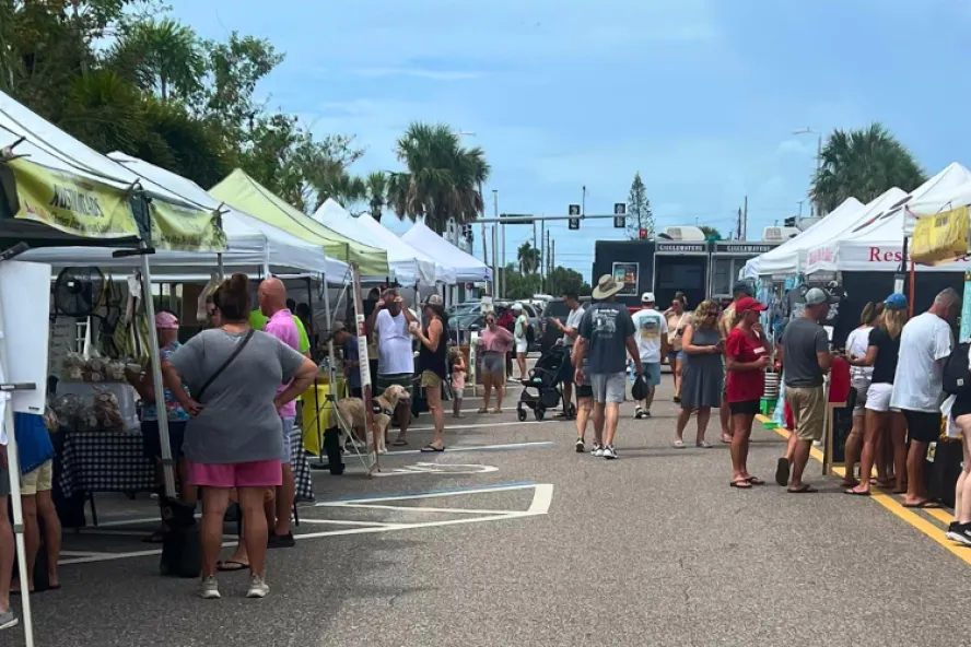 People at an outdoor market shopping around various white tents.
