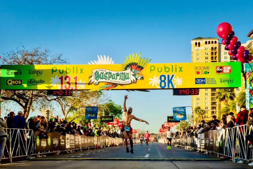 a happy runner crosses the finish line at Gasparilla Distance Classic