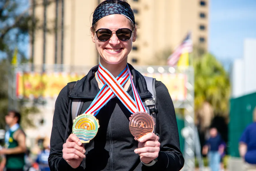 a smiling woman displaying two medals from the St. Petersburg Distance Classic