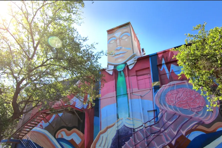 A colorful mural of a man in a suit painted on a wall of a tall building in Florida.