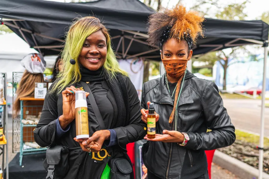 Two women wearing black outfits holding bottled products smiling.