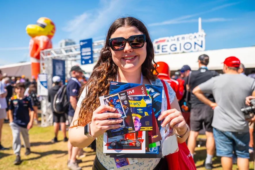 a smiling fan holding "swag" collected at the fan village at the Firestone Grand Prix
