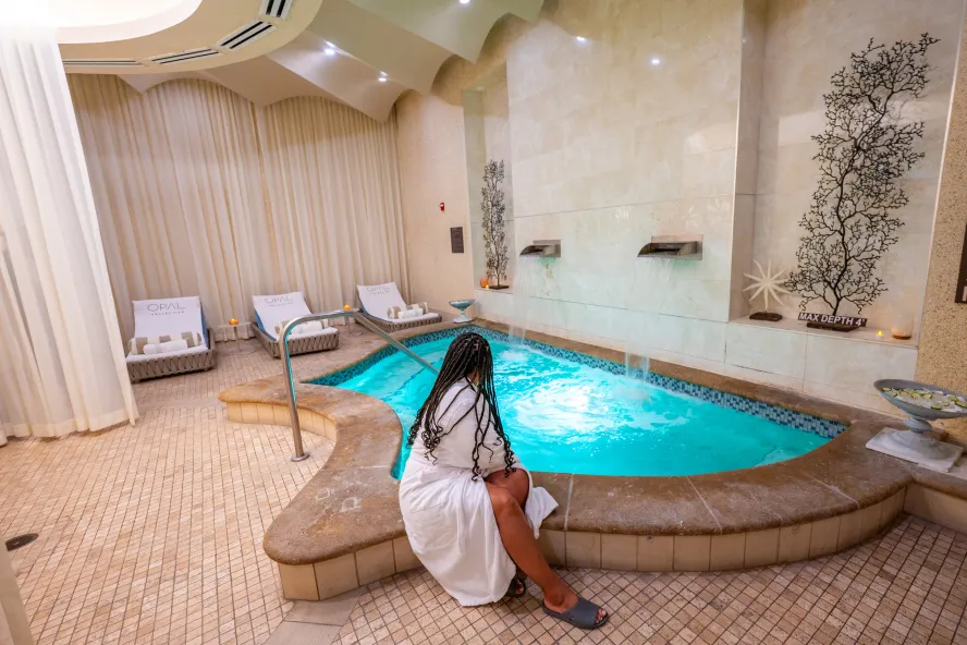 a woman in a spa bathrobe sitting on the edge of a small pool indoors at Opal Spa at Sandpearl Resort