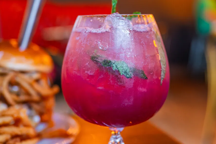 a bright pink cocktail with mint leaves next to a decadent burger at Gigglewater's