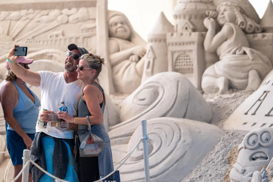 a couple taking a selfie in front of a giant sand sculpture at the Pier 60 Sugar Sand Festival