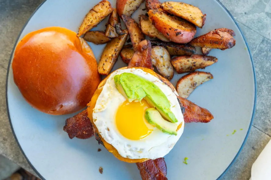 a sunnyside egg with avocado on a brioche bun next to thick potato wedges at Clear Sky Cafe in Clearwater FL