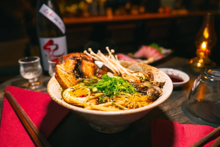 a bowl with asian inspired cuisine, with sake on the table behind it, at In-Between Days in St. Pete
