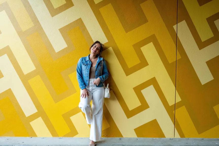Yasmin, a local travel influencer, leaning on a yellow mural with a geometric design made up of the letter H, at the Hollander Hotel in St. Petersburg FL