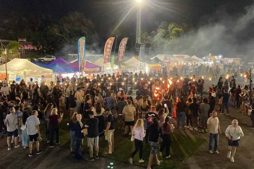 Outdoor evening market featuring a crowd of people with surrounding vendor tents.