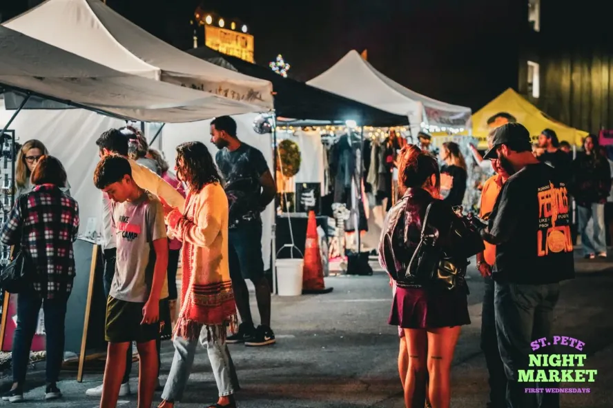 St. Pete Night Market featuring people shopping around vendor tents at night. 