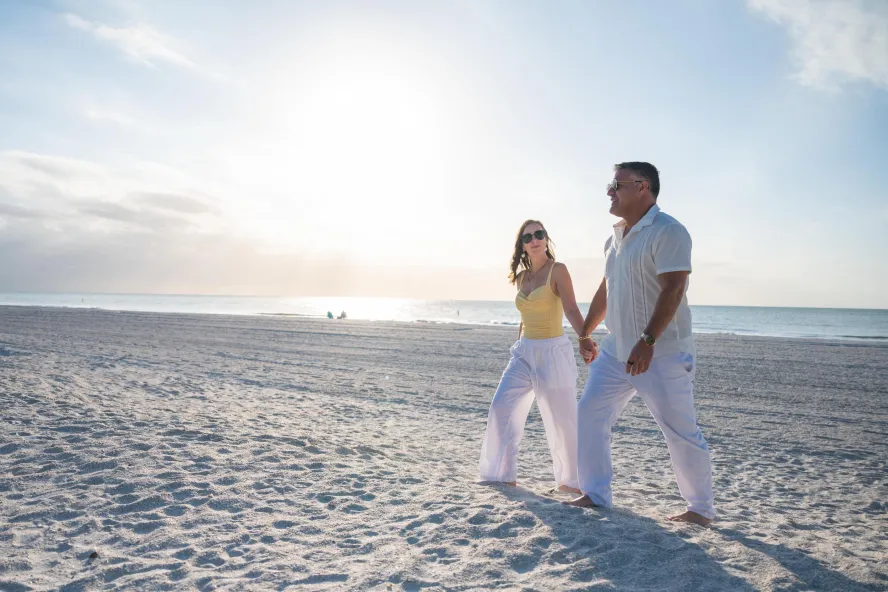 a couple walks holding hands on a white sand beach in St. Pete-Clearwater