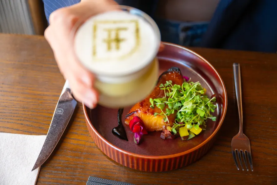 a plate of miso black cod and someone's hand holding an elegant cocktail at Fortu in St. Pete