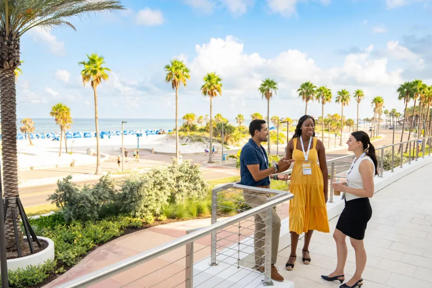 three meeting attendees chat on a outside patio overlooking the beach at Opal Sol in Clearwater Beach