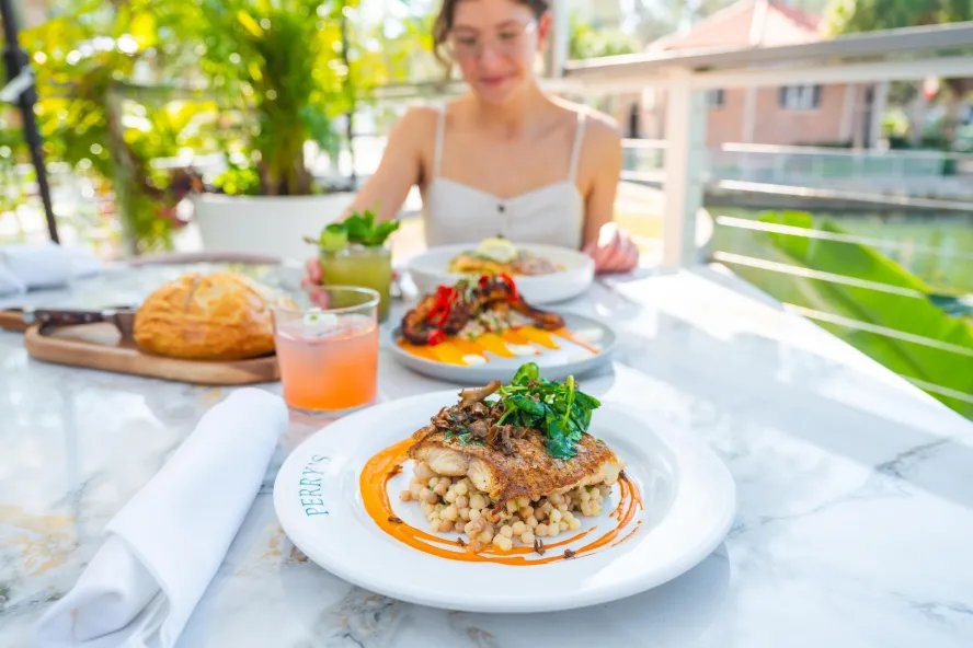 a woman dines outside at Perry's porch with lush greenery near the table