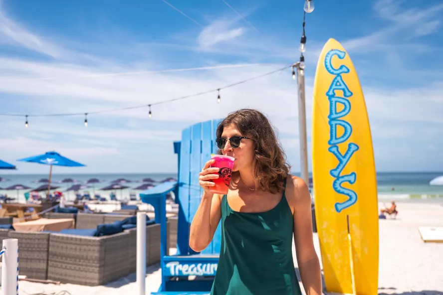 a woman sips a red drink on the beach at Caddy's Treasure Island