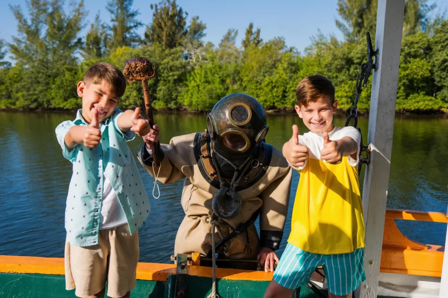 two kids pose with a diver dressed in traditional gear on the St. Nicholas Boat Lines in Tarpon Springs