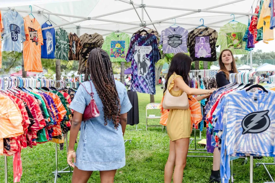Women shopping for clothes at an outdoor flea market.