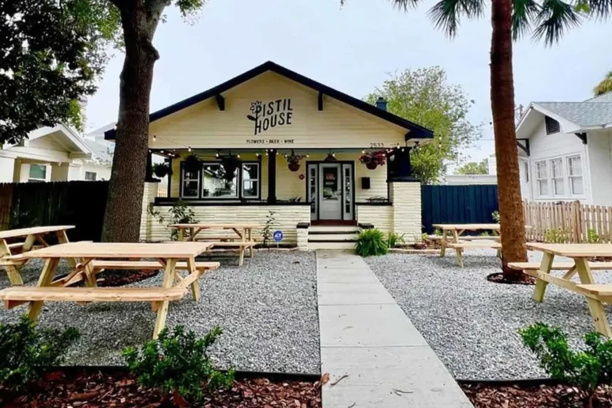 Exterior of Pistil House, a bungalow-style restaurant with picnic tables and palm trees in its outdoor seating area.