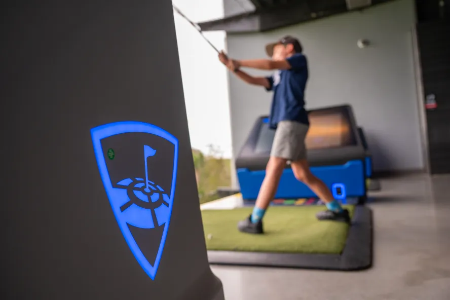 Golfer swings a club from an indoor golf simulator bay.