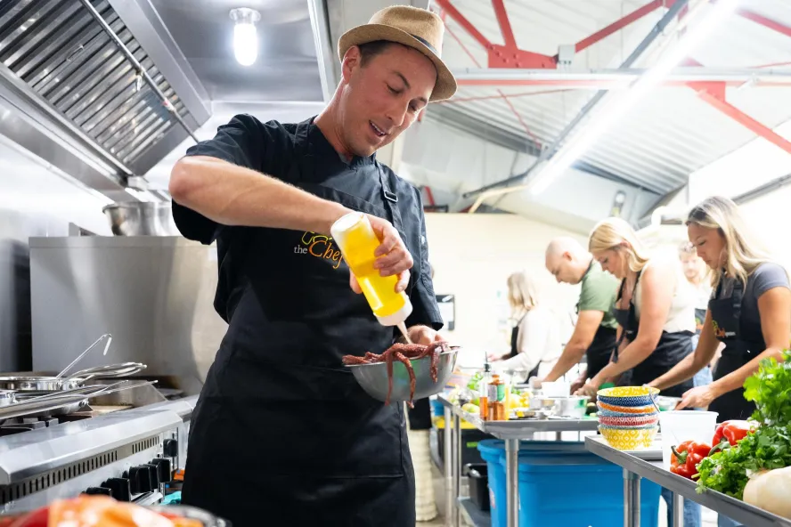 a chef adds oil to a bowl while students work in the background at a cooking class with The Chef Upstairs