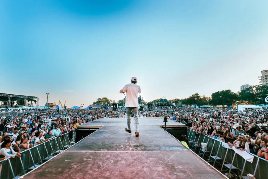 Performer on stage at St. Pete Country Music Fest with a large, festive crowd.