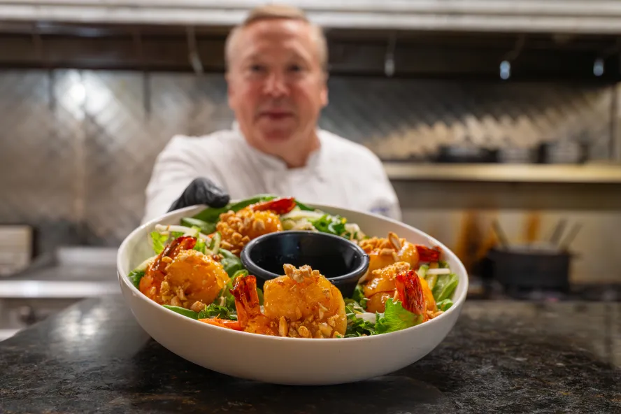 a chef sends out a salad with shrimp from the kitchen at Grace Restaurant in St. Pete Beach