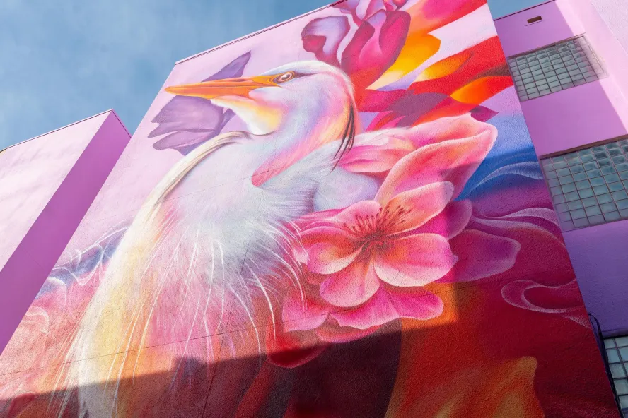 “Abiding Light” by artist Dreamweaver (Taylor Smith), a vibrant mural featuring a white heron surrounded by pink, red and orange flowers in St. Petersburg, Florida.