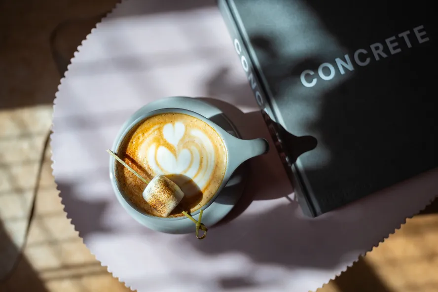 A latte with heart-shaped foam art and a toasted marshmallow sits beside a Concrete coffee table book.