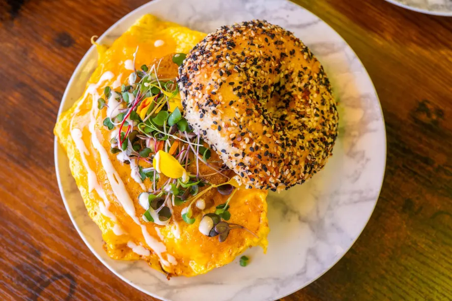 An everything bagel breakfast sandwich with melted cheese, eggs, microgreens and a drizzle of sauce at Southie Coffee.