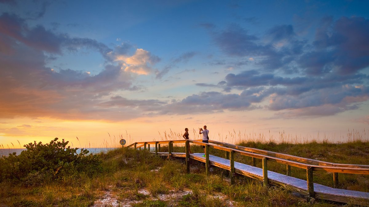 Um casal tirando fotos durante o pôr do sol em uma passarela na bela Pass-a-Grille Beach perto de St. Pete Beach, Flórida