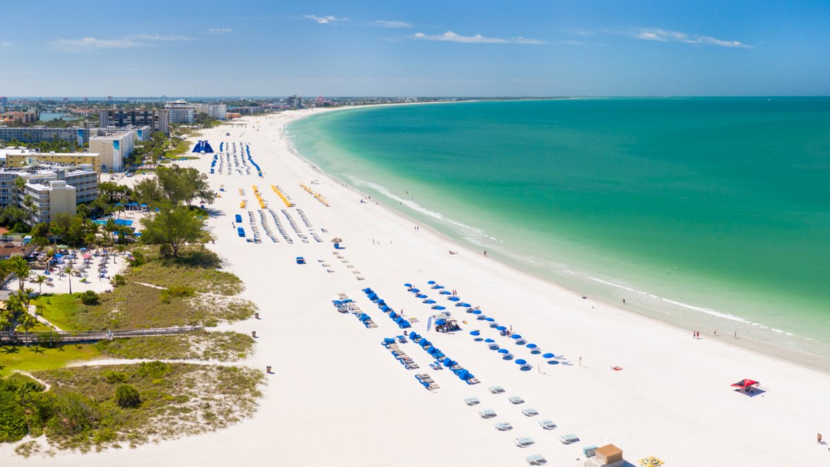 Vista aérea de St. Pete Beach pelo norte, incluindo areia branca, água azul e cabanas sombreadas.