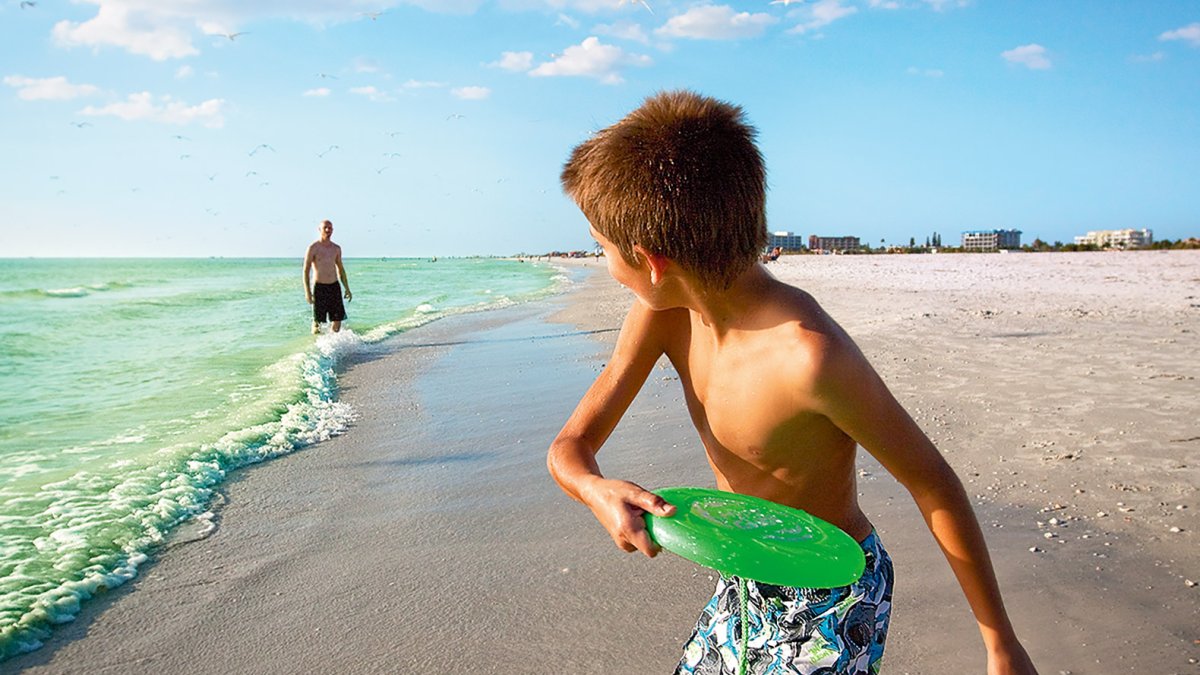 A boy playing frisbee with his dad in on the beach in Treasure Island near St. Pete Beach