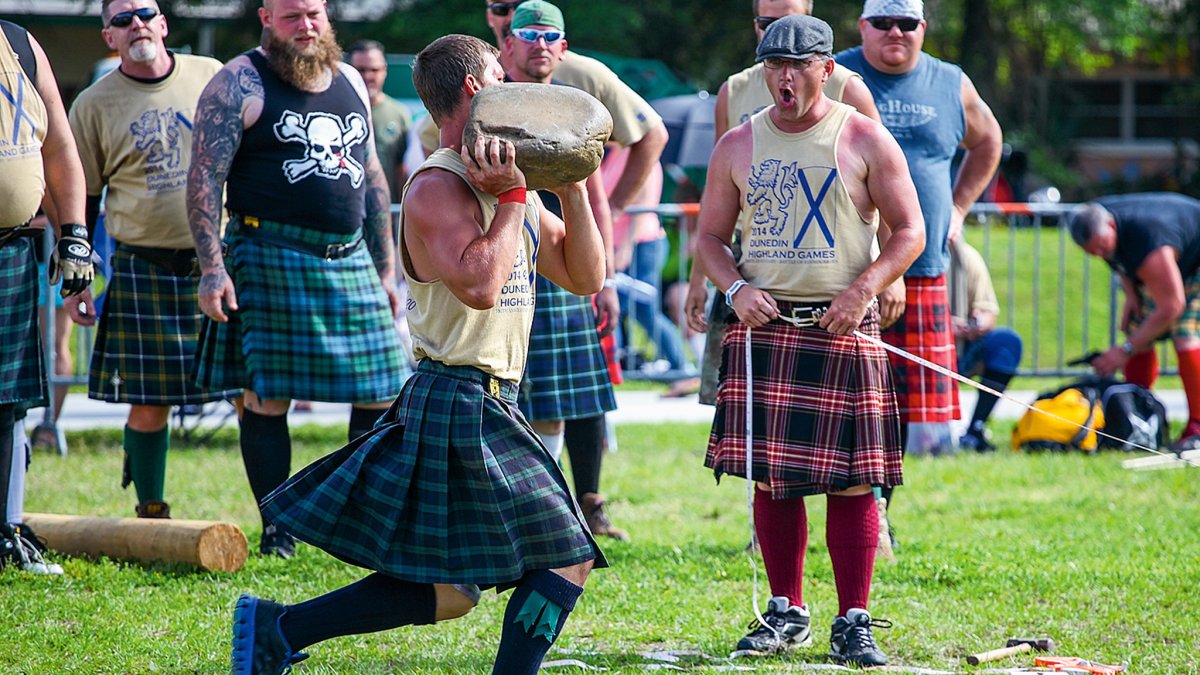 um jovem de kilt joga uma pedra enquanto a multidão aplaude nos Highland Games de Dunedin