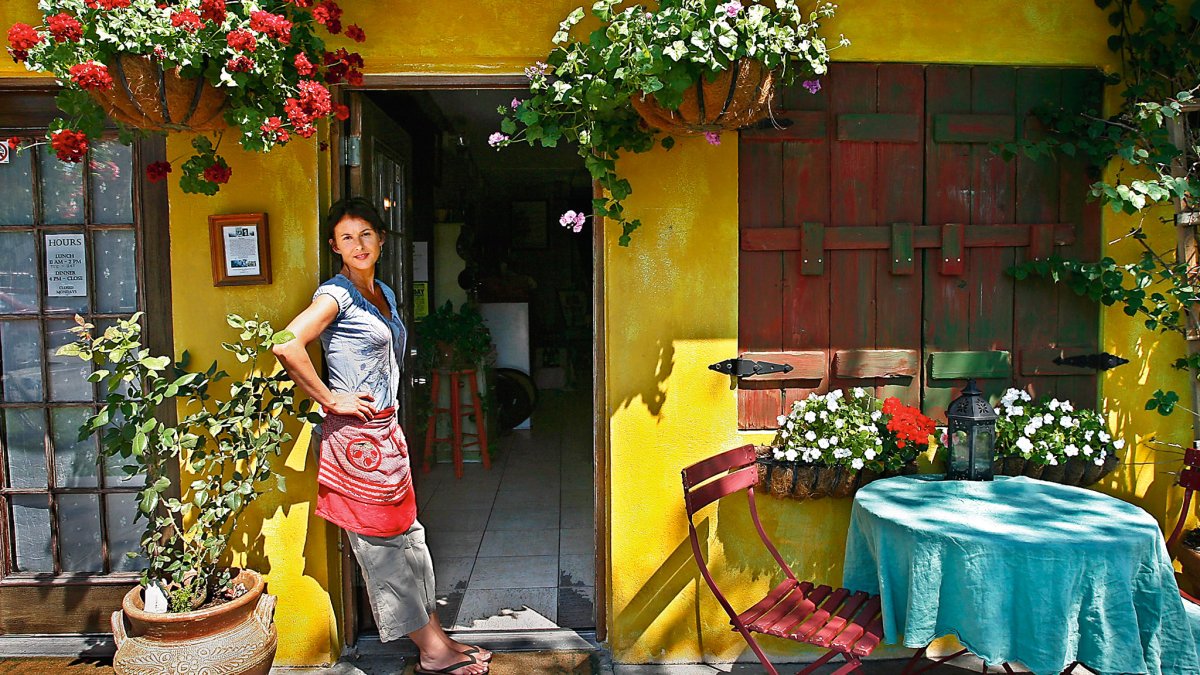 a smiling server waits at the entrance of Pia's Trattoria, a cozy Italian restaurant in Gulfport; the building is painted bright yellow and a table is outside