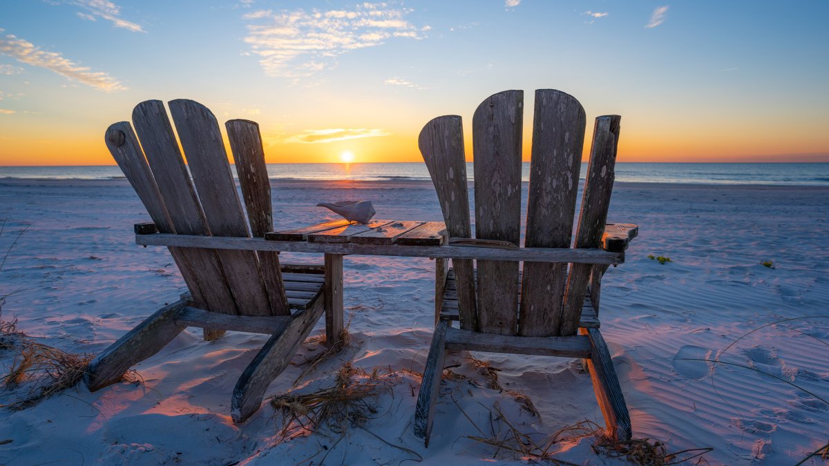 Two Adirondack chairs facing the Gulf waters at sunset in Pass-a-Grille Beach during sunset