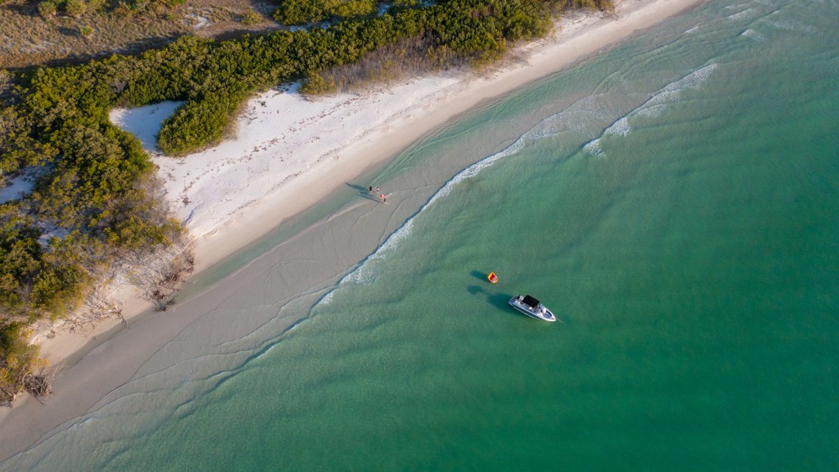 Aerial view of a boat anchored off the beach at Shell Key Preserve; dunes border the beach and the Gulf water is emerald green